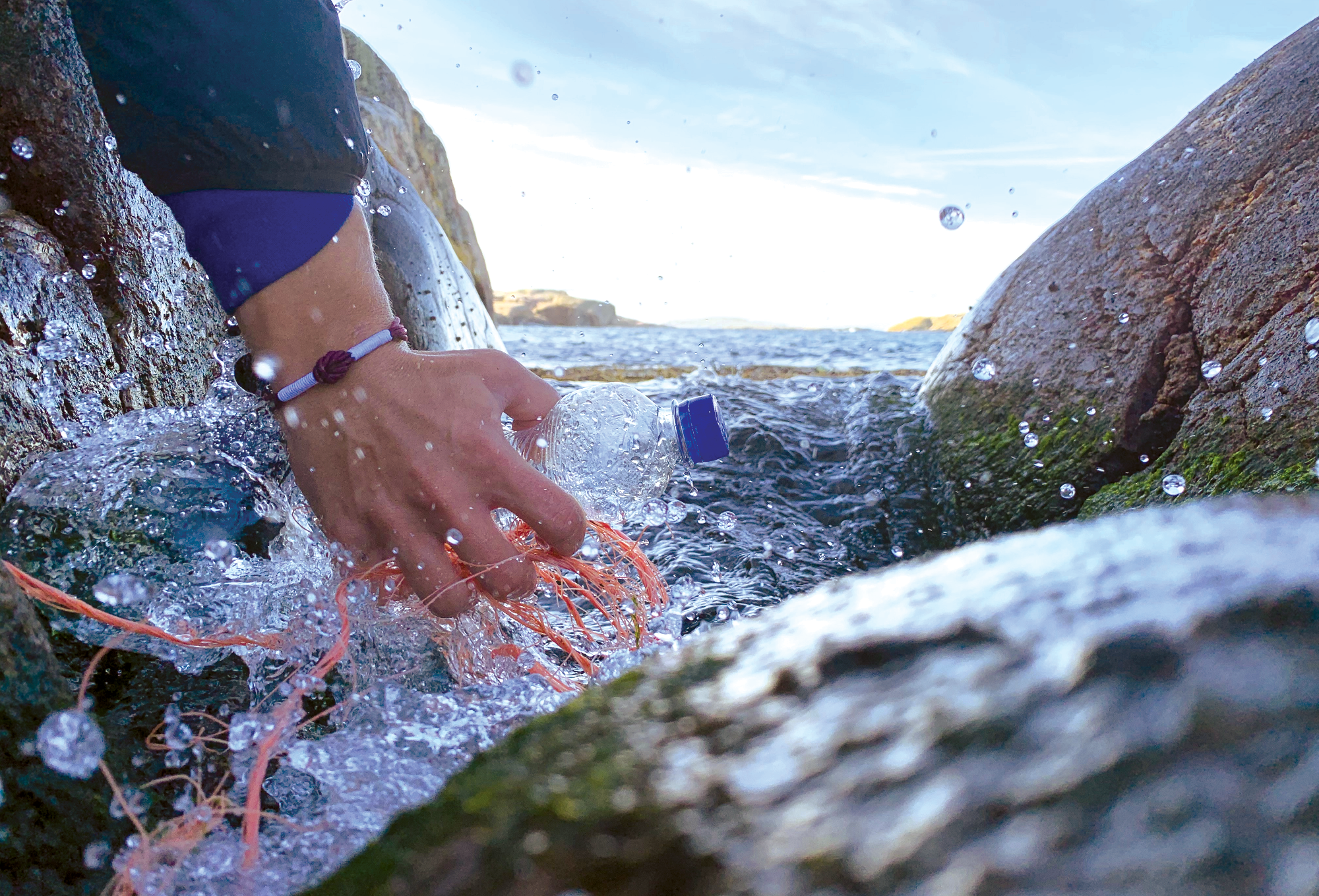 Hand in the ocean waves cleaning up trash.